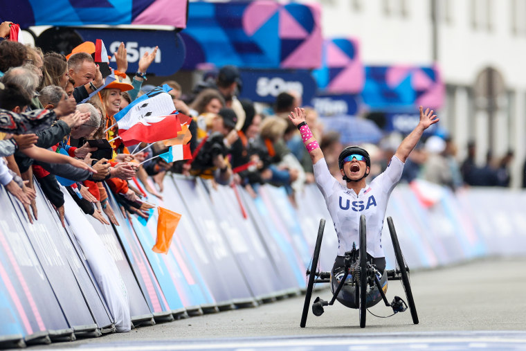 Oksana Masters celebrates as she finishes a cycling race next to a crowd of onlookers