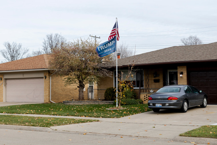 A Donald Trump flag and an American flag fly outside on the front lawn of a home, a car is seen in the driveway