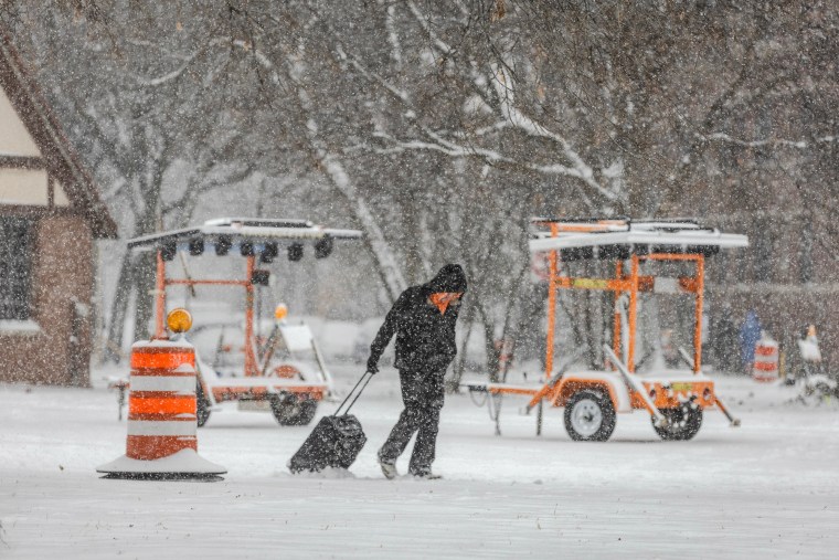 A person walks through the snow with a suitcase as snow falls