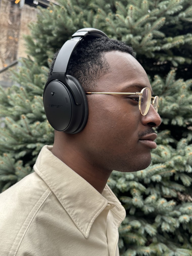 A man with glasses wearing the Bose QuietComfort headphones outside with trees in the background.