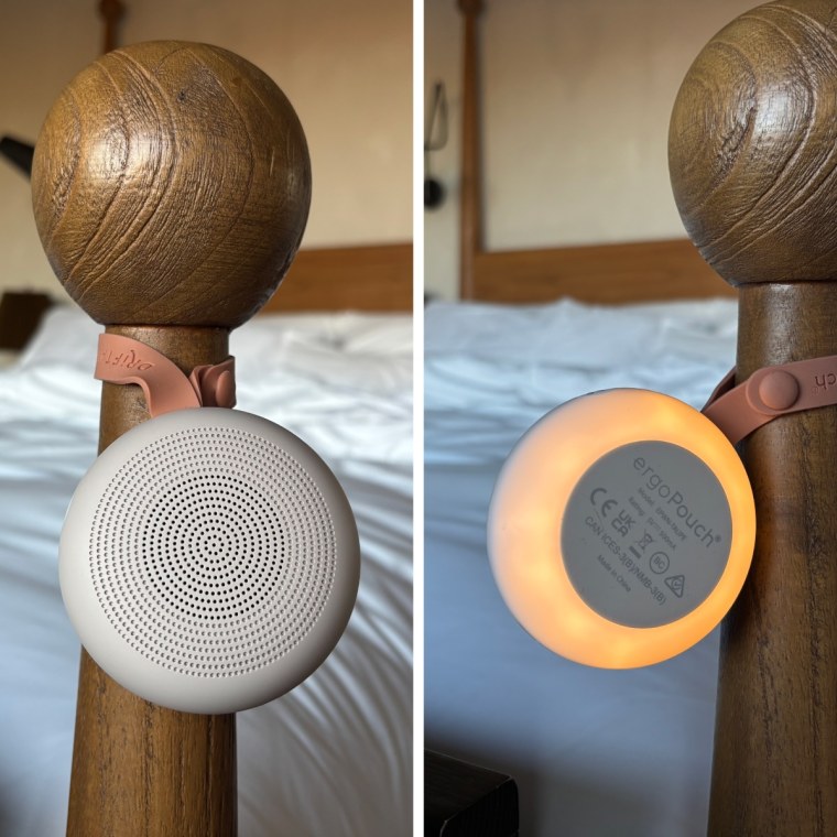 The ErgoPouch Drift Away White Noise Machine hanging on the pole of a wood bed frame.