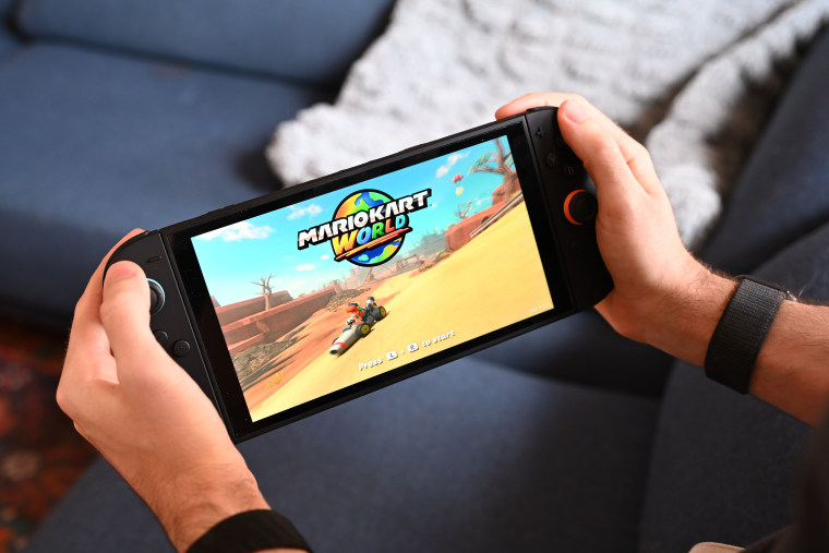 A man holding the Nintendo Switch 2. On the screen is the Mario Kart World title screen.