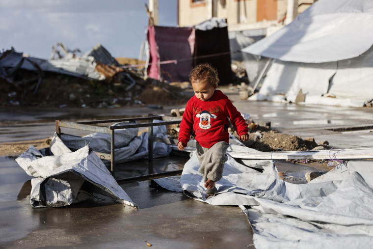 A toddler walks outside on destroyed tent material
