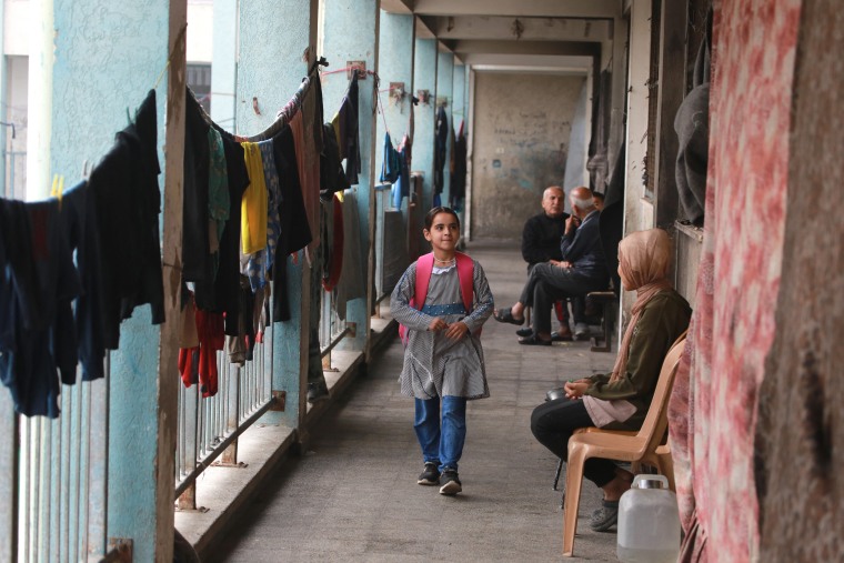A Palestinian girl walk to a classroom, as displaced adults sit near hanging laundry watching, at the UNRWA Deir al-Balah Joint School, west of Deir al-Balah, in the central Gaza Strip on Dec. 6.