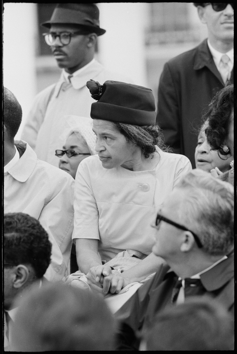 Rosa Parks speaks at a podium outside as people stand behind her