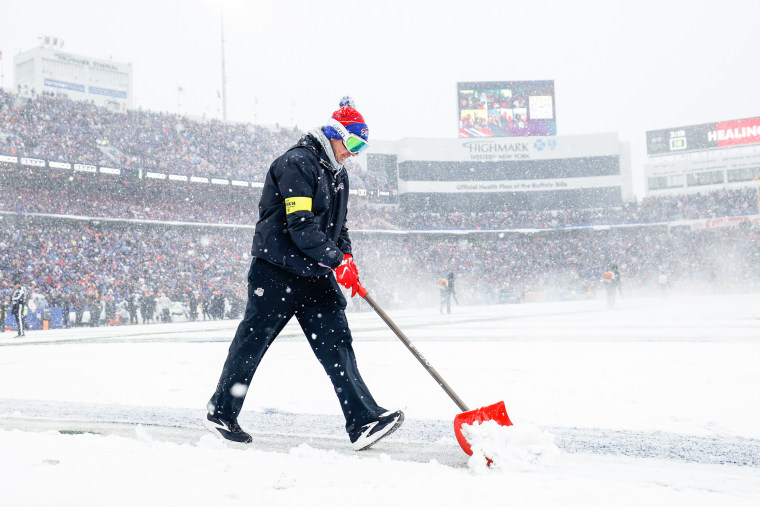 A person shovels snow on a football field