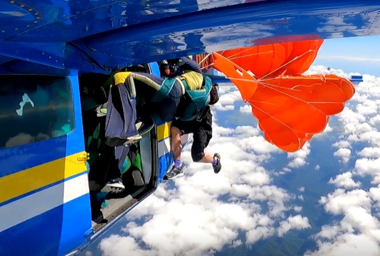 Two people grip the side of a plane in the air as a parachute gets stuck to a plane wing
