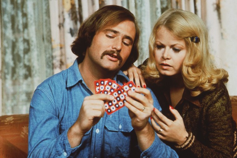 Rob Reiner e Sally Strather, como o casal Mike e Gloria Stevic, assistem a um jogo de cartas em cena de episódio da série de televisão 