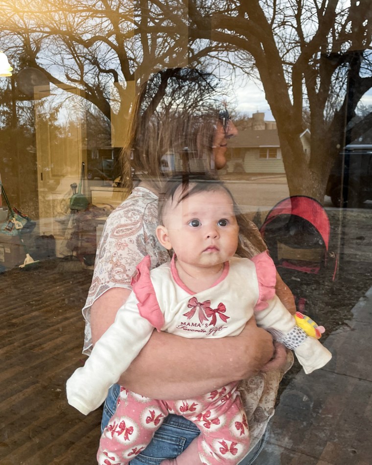 A mother holds her daughter, as seen through the glass window of a door, the outside can be seen reflected