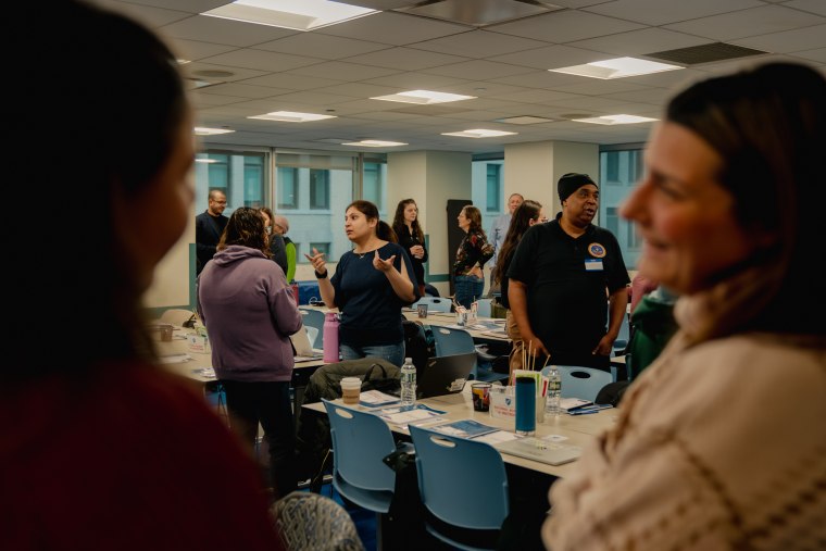 People talk to each other while standing inside of a classroom