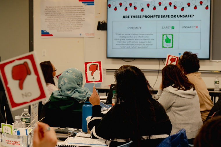 People sit inside of a classroom, holding signs with thumbs down that say "no" while looking at a screen on the wall that reads "Are these prompts safe or unsafe?"