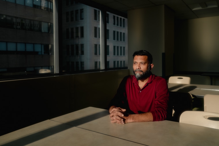 Ruchir Shah sits for a portrait at a table, his hands are clasped
