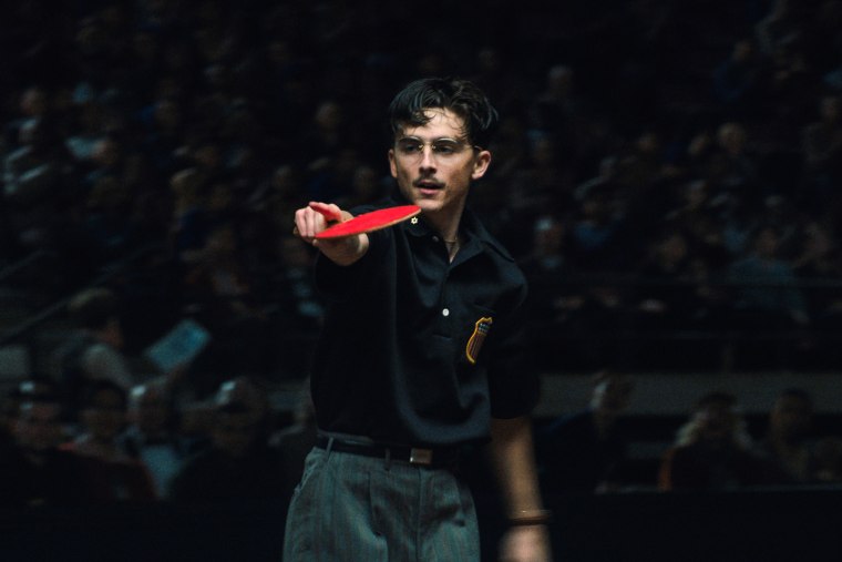 Timothee Chalamet holds a ping pong racket and points with it