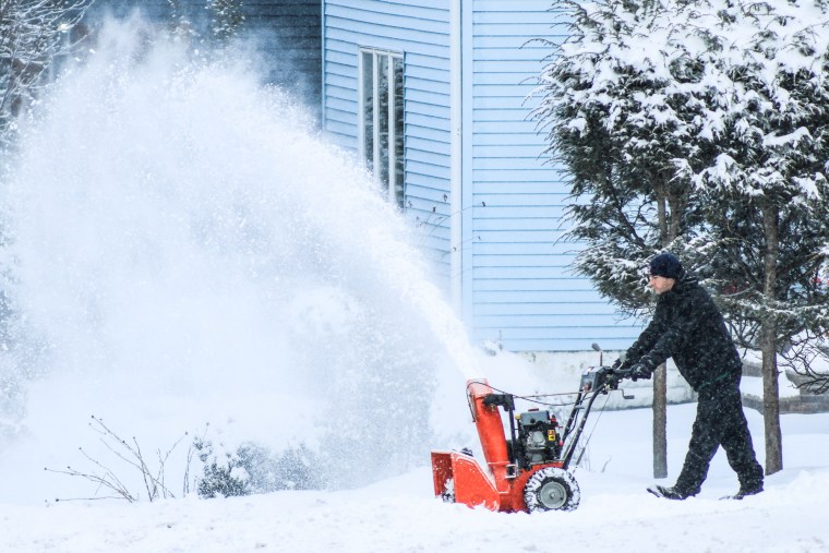 A man removes snow with a snowblower outside