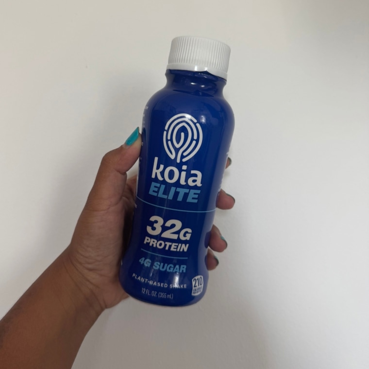 Woman holding Koia Elite protein shake against white wall