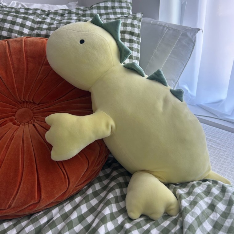 Dinosaur stuffed animal laying on checkered bed sheet