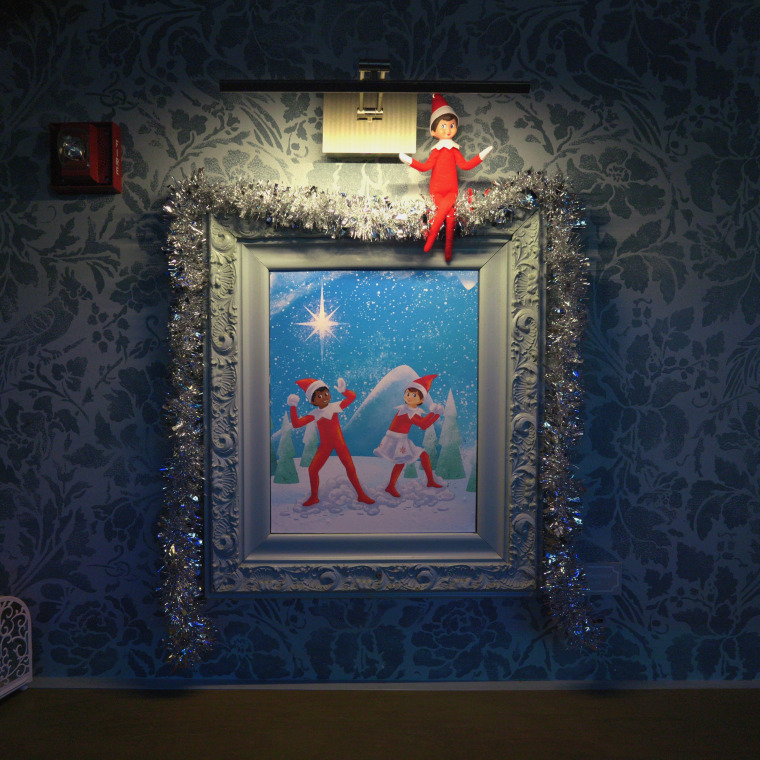 An Elf on the Shelf perches atop an original painting by Morris Shepphard.