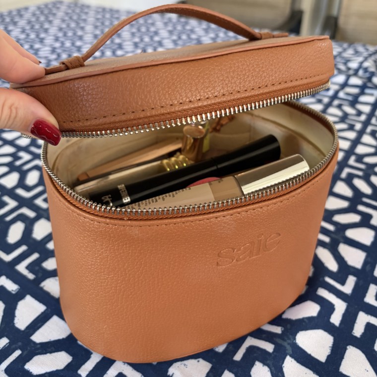 Woman holding open Saie toiletry bag with makeup inside