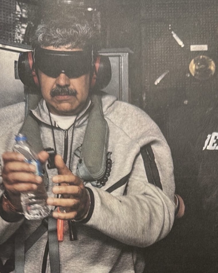 Nicolas Maduro, blindfolded and wearing headphones, stands while holding a water bottle