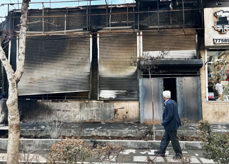 A man passes a burned-out national supermarket chain store in Tehran on Thursday.