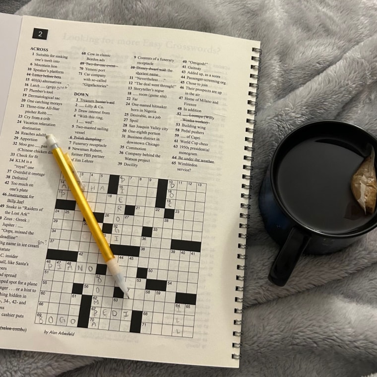 A picture of a crossword puzzle with a pencil, next to a cup of tea, on a grey blanket.