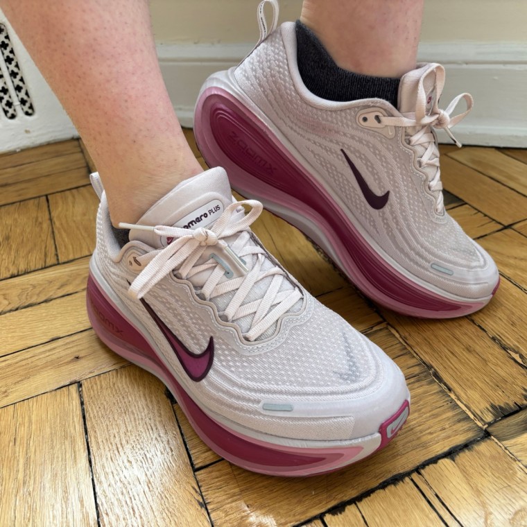 A person wearing a pair of pink Nike Vomero Plus women’s running sneakers.