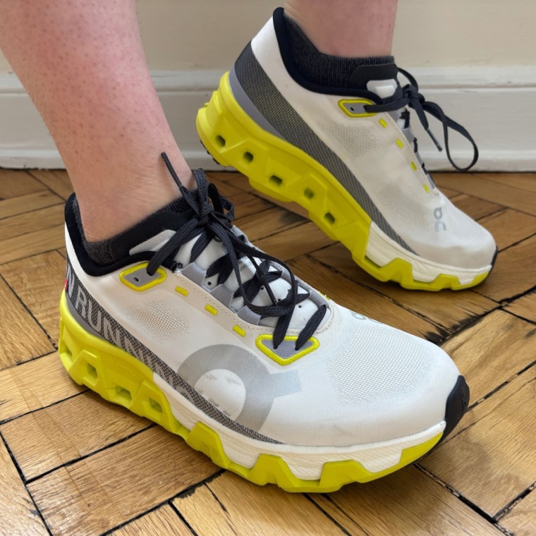 A person wearing a pair of white, green and black On Cloudmonster Hyper women’s running sneakers.