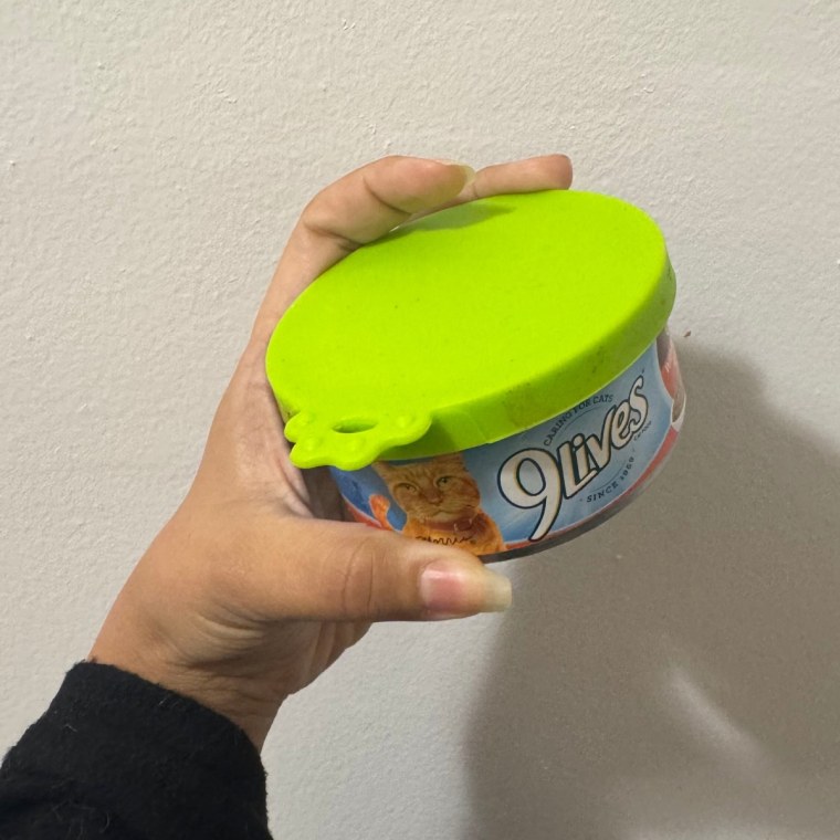 Photo of a hand holding wet cat food with a Comtim Silicone Can Lid against a white wall.