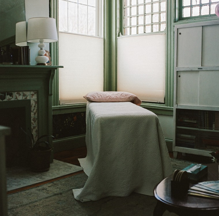 A medical recliner covered in a blanket with a pillow on top can be seen in the corner of a living room