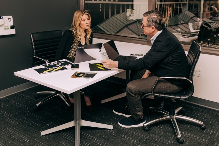 Leigh Anne Clark, left, and Dave Clark sit across from each other at a table with paperwork and their laptop while speaking