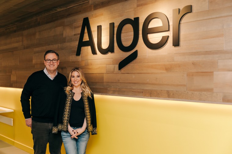 Dave Clark, left, and Leigh Anne Clark stand near a wall displaying the company's name Auger on a wooden facade wall behind them