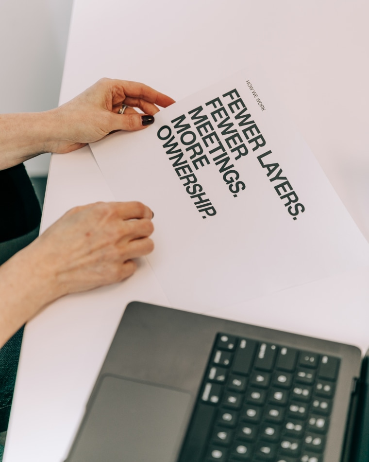 Hands hold a document that reads "How we work
Fewer Layers.
Fewer Meetings.
More Ownership."