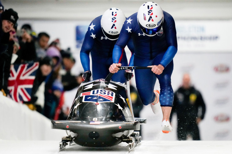 Frank Del Duca dan Charles Volke mendorong kereta luncur di jalur es di samping penonton