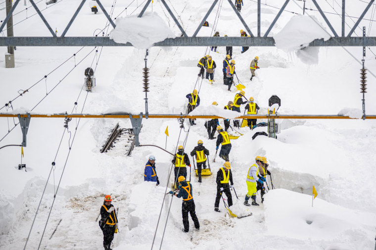 Staff members shovel snow covered rail tracks at Shin Aomori station.