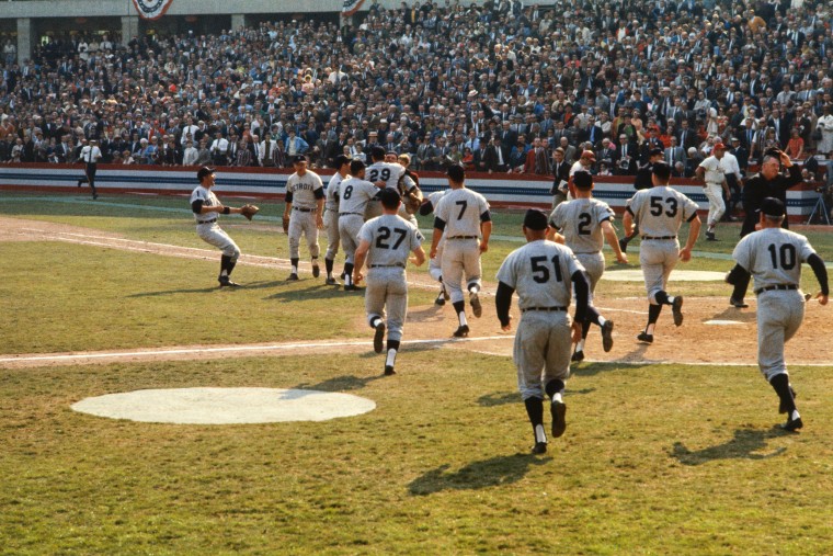An old color photograph showing baseball players rushing out onto the field in celebration.