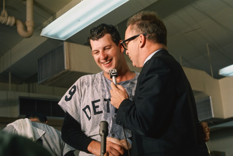 Mickey Lolich smiles while a reporter holds a microphone up to his face. 