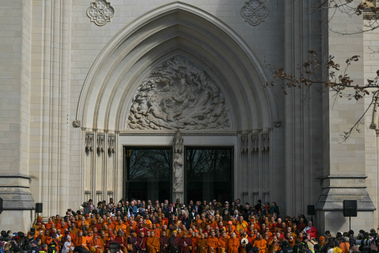 Buddhist monks stand in front of the Washington National Cathedral while wearing orange gowns.