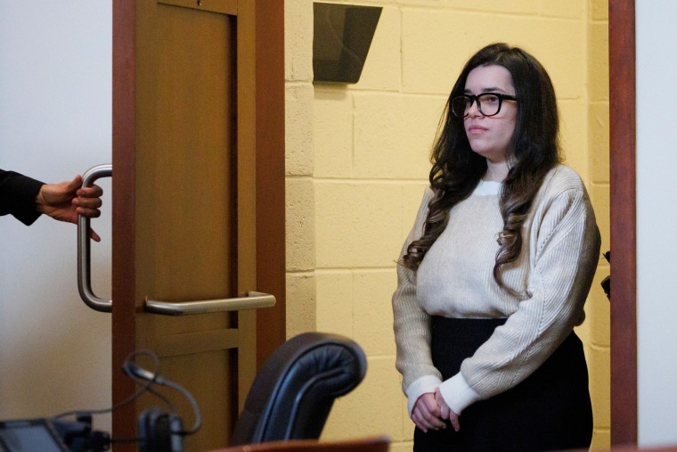 Juliana Peres Magalhães standing by a door while holding hands.