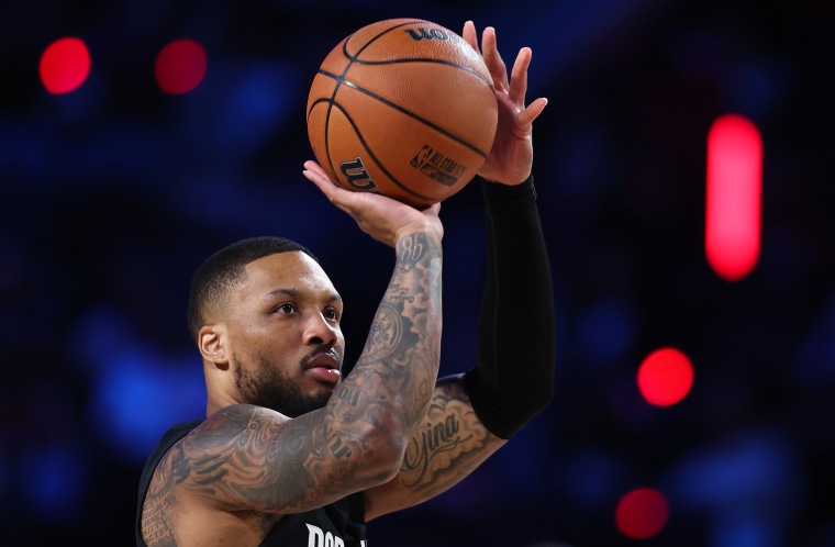 Damien Lillard holds a basketball above his head in his right hand, poised to shoot a basket.