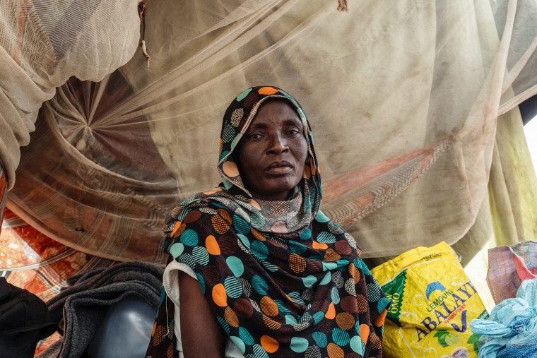 A woman wearing a colored headscarf gazes directly into the camera with a somber expression.