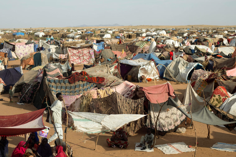 Hundreds of makeshift shelters made of blankets, tarps, and sticks extend into a desert landscape.