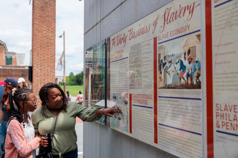 A person points at exhibit signage on a wall next to a young child