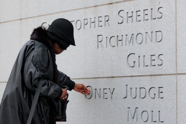 A woman places a hand on a stone wall with names engraved