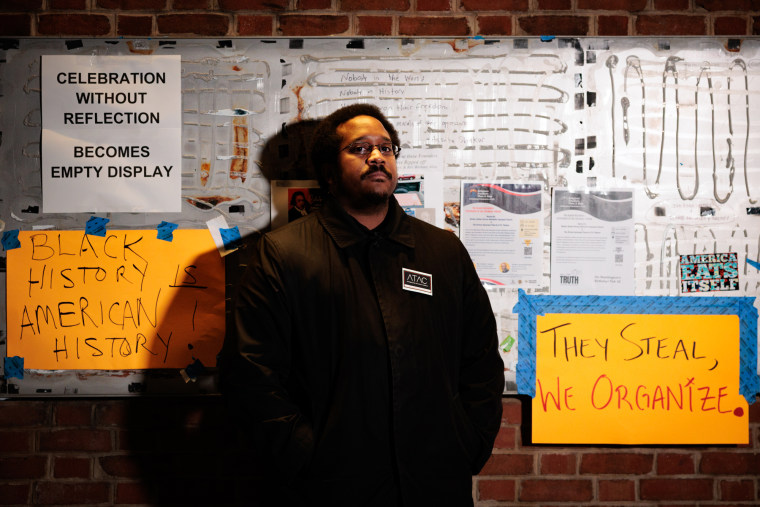 Mijuel K. Johnson stands against a brick wall with posters for a portrait