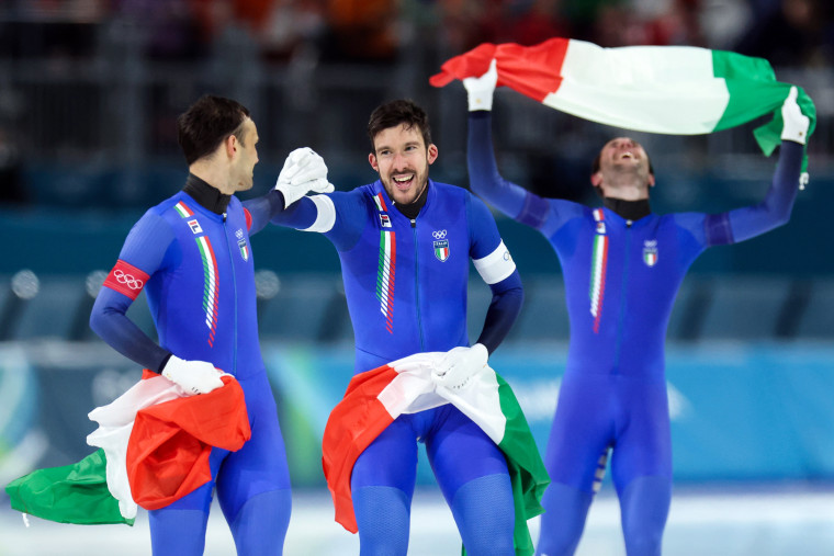 Andrea Giovannini and Davide Ghiotto hold hands and Italian flags on the ice