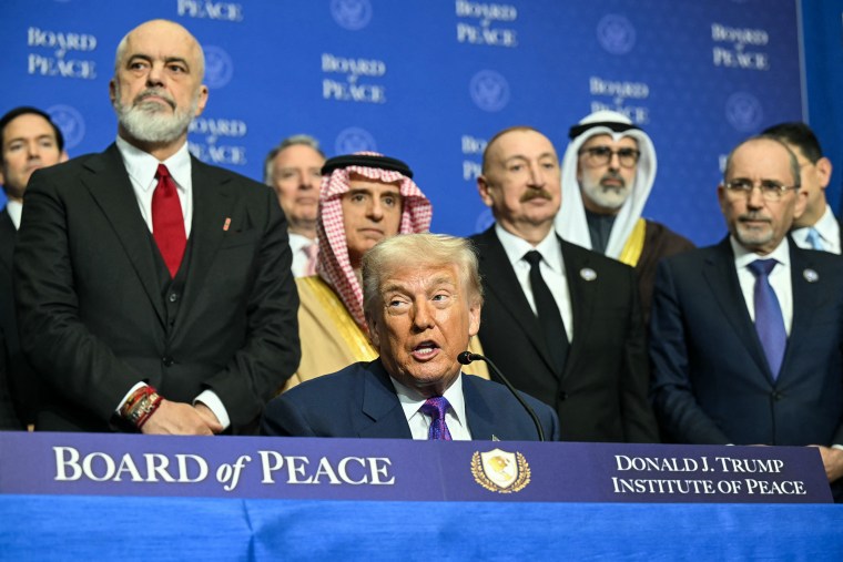 Donald Trump speaks while seated at a table with signage reading BOARD OF PEACE.