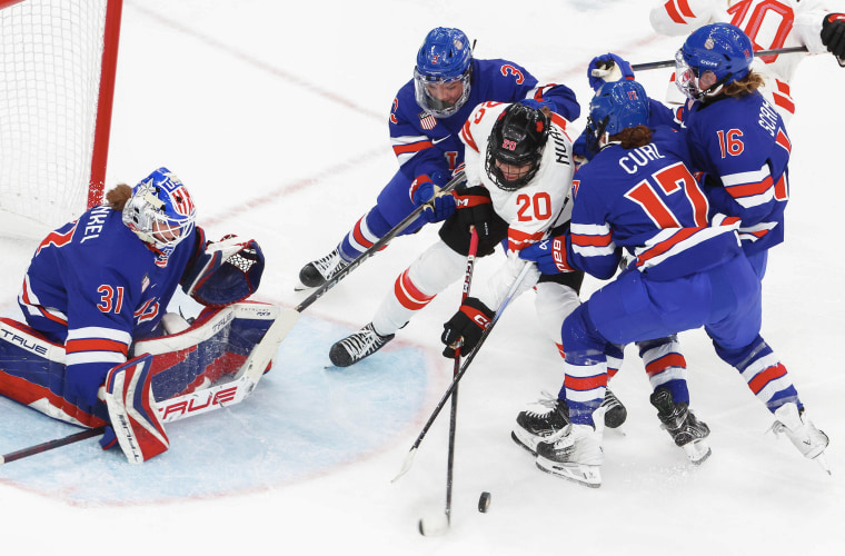 Ice hockey players battle in a tight scrum in front of the net.