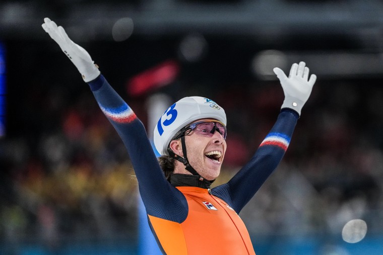 Jorrit Bergsma smiles with both hands in the air. He's wearing a helmet and spandex racing uniform.