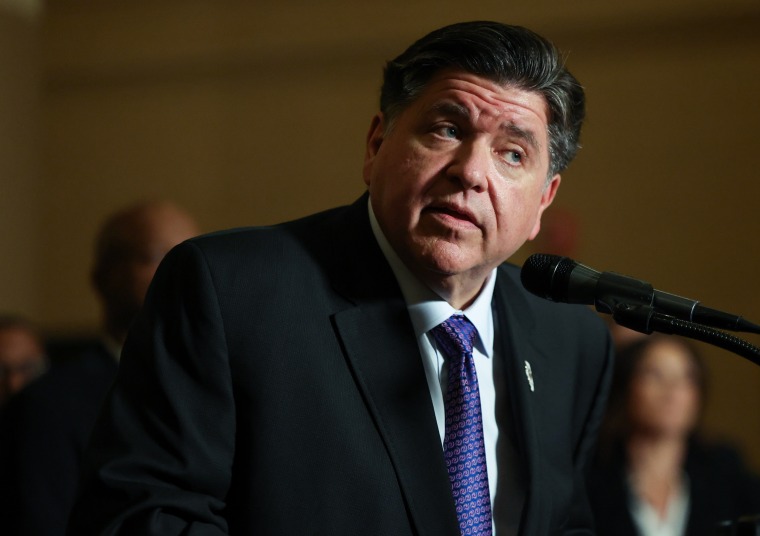 JB Pritzker stands at a microphone and gazes to the side.