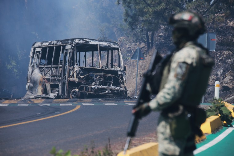 A soldier stands guard by a charred vehicle after it was set on fire, in Cointzio, Michoacán state, Mexico, Sunday, Feb. 22, 2026, following the death of the leader of the Jalisco New Generation Cartel, Nemesio Oseguera, known as "El Mencho."